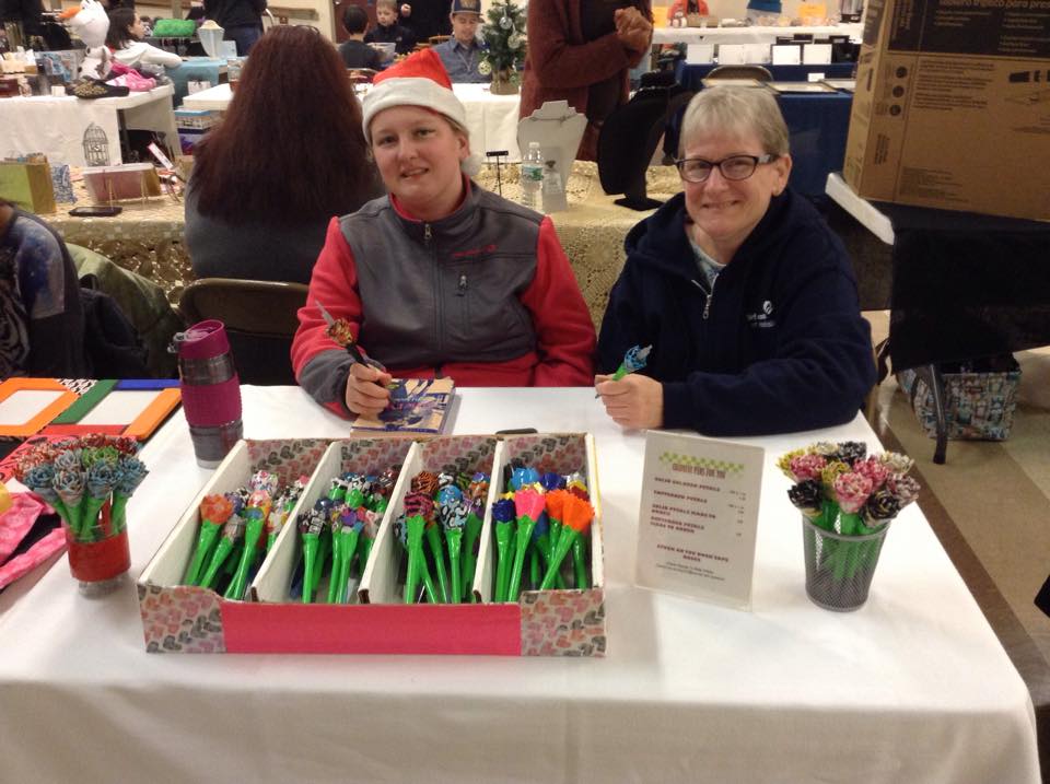 Two ladies sitting at a table selling pens
